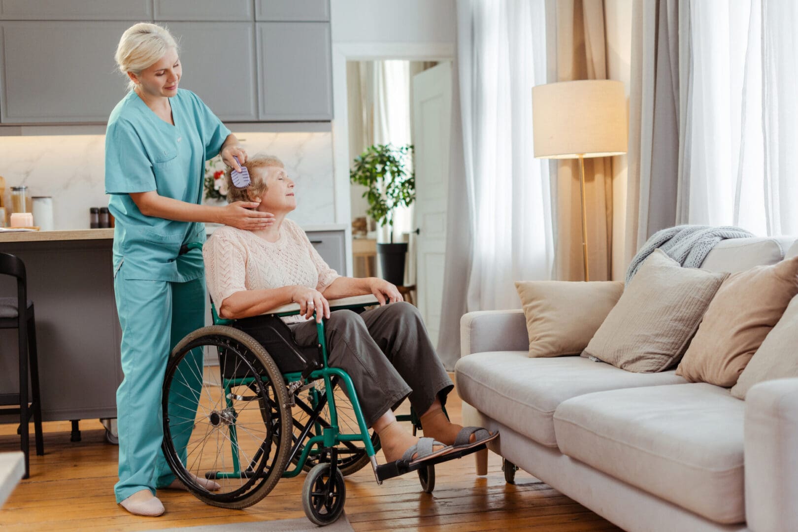 Nurse in scrubs gently brushes the hair of a senior woman in a wheelchair at home. Showing compassion and support. Health care concept