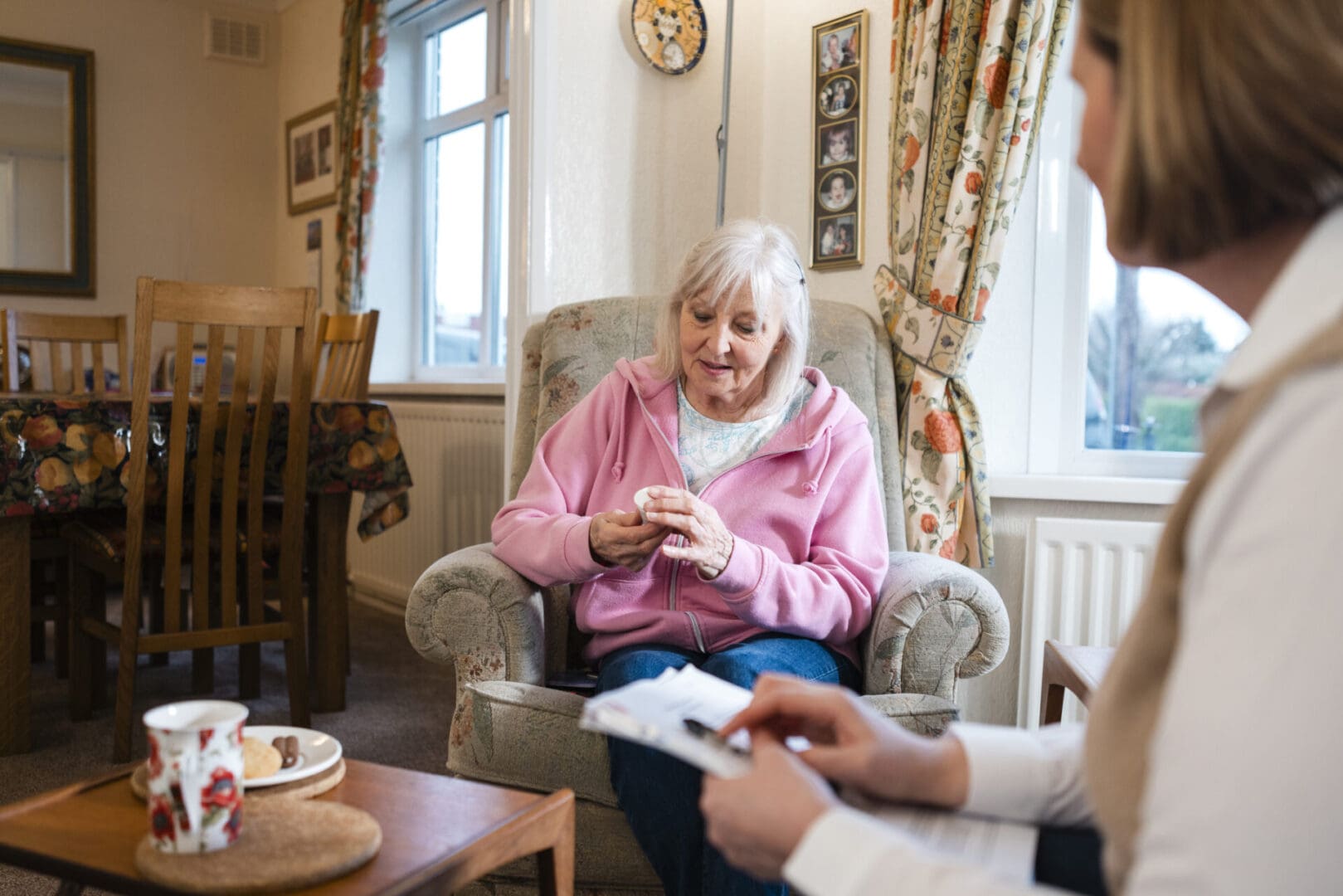 Senior woman sitting in a living room being visited by a community outreach volunteer in the North East of England. The volunteer is sitting talking to her holding leaflets, giving her medication to look at.